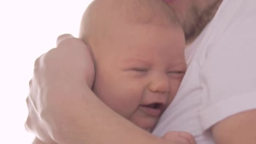 Close-up of a crying baby's face as the father tries to console his child.