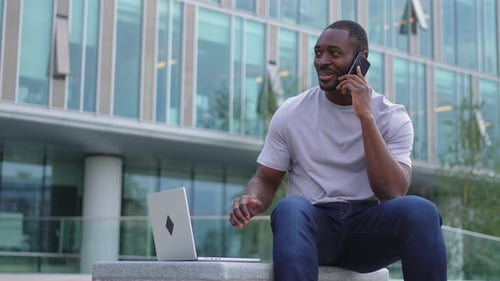 African American Man Freelancer Using Laptop Talking on Phone on Urban Street in City Business Man