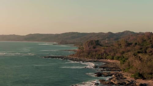 Drone parallax flight above breaking swell in empty Costa Rica bay in sunset