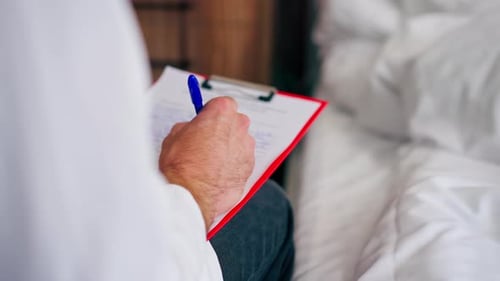 Close-up shot of a male doctor's hand with ring on his finger filling out patient's medical history