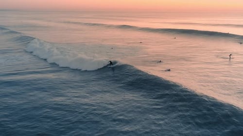 Beautiful aerial view of a professional surfer surfing a perfect wave on a sunset / sunrise.