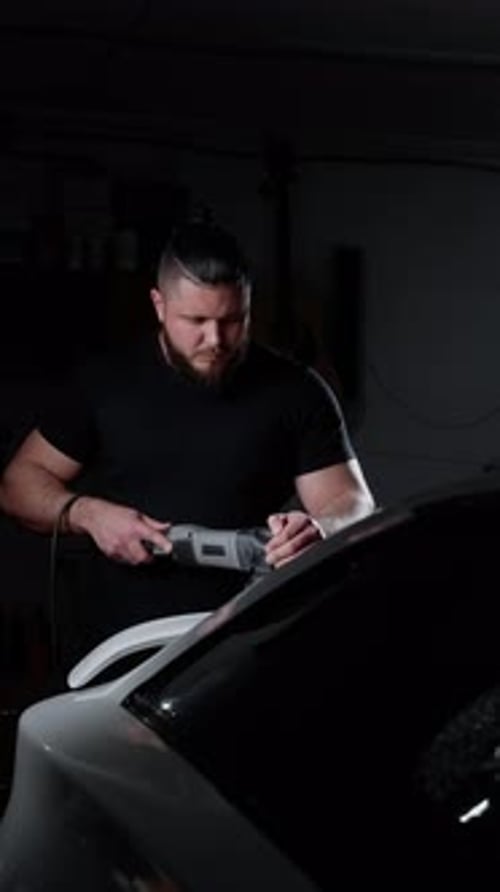 Man Polishing a Gray Car in a Dark Garage