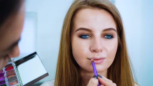 Closeup Female Makeup Artist Doing Professional Makeup for Young Red Hair Woman at Beauty Salon