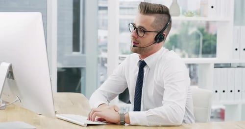4k video footage of a young businessman wearing a headset while working on a computer in an office