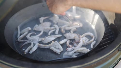 Squid sizzling in skillet being cooked outdoors