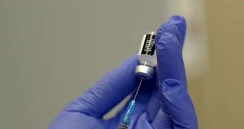 The doctor in protective gloves holds a syringe and a vaccine bottle for coronavirus treatment