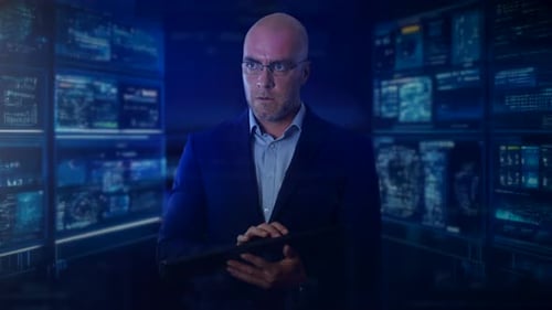 An computer programmer using a keyboard, standing in front of multiple screens. The man is programmi