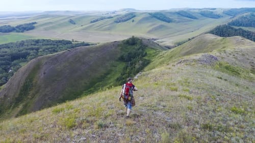 Middleaged Male Tourist with a Large Backpack Walks Along a Hilly Ridge Enjoying Beautiful Views