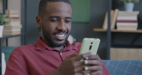 Smiling Man Using Phone on Couch Indoors