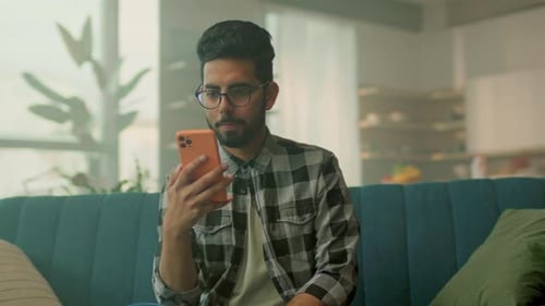 Man Using Smartphone Sitting on Blue Couch Indoors