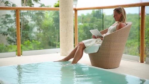 Woman uses digital tablet by sparkling pool at tropical cancun resort Mexico