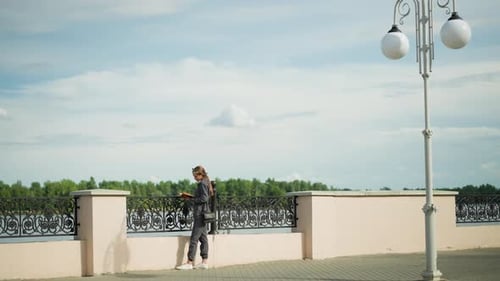 Lady in Grey Reads By Riverfront Fence with Scenic Trees and Lamp Post