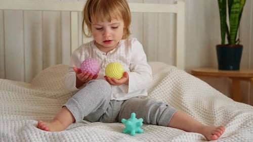 Young Child Playing with Colorful Textured Balls on Bed
