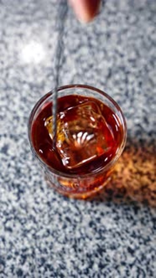 Brown drink with a big ice cube mixed with a long spoon. Preparation of a beverage in the bar.