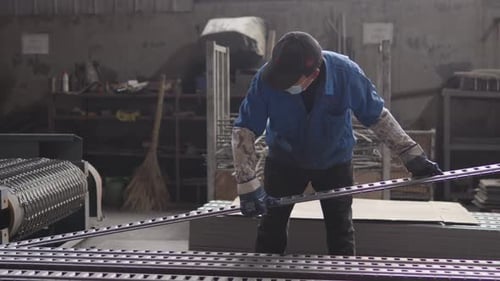 Factory Worker in Blue Uniform and Gloves Performing Physical Labor Handling Items on Manufacturing