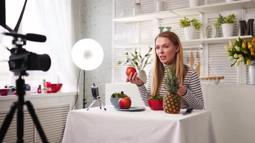 Un bloguero gastronómico cocinando ensalada vegana fresca de frutas en un estudio de cocina, tutorial de filmación ante la cámara para