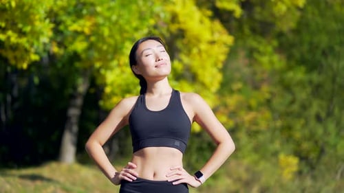 Close up portrait young happy asian woman standing in nature between forest trees relaxes, breathes