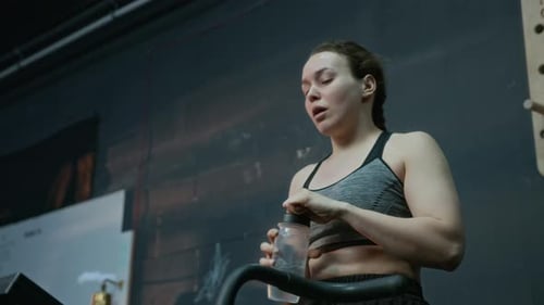 Girl Pausing Cardio Workout on Cross-trainer to Drink Water in Gym