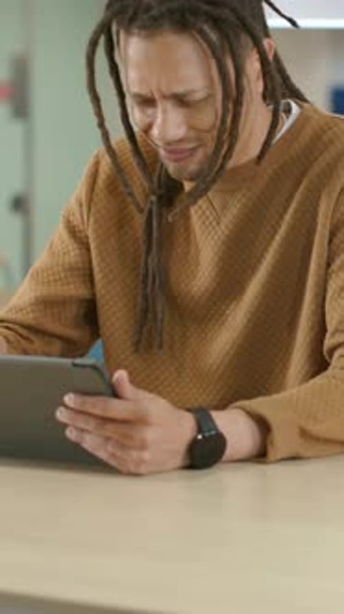 Vertical video: Reacting to odd screen dreadlocked man in sweater tapping tablet at cafe calming