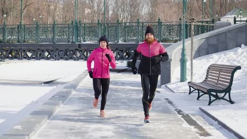 Cheerful people wearing pink and black sportswear running together in winter park in slow motion
