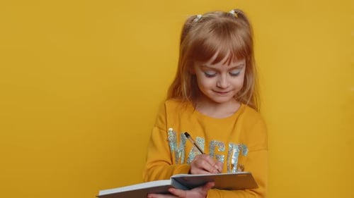 Child Writes in Notebook on Yellow Background