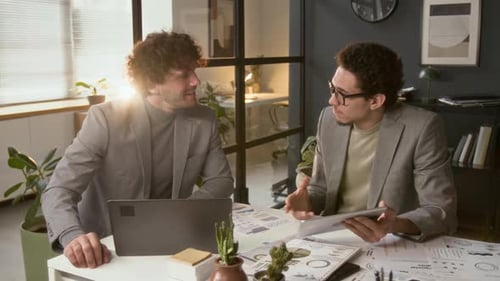 Two Young Businessmen Discussing Investment Opportunities at Office Desk