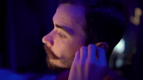 Man Inserts Wireless Earbud in Blue Lighting