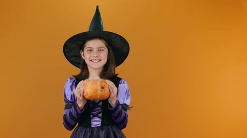 Girl in Witch Costume Holds Halloween Pumpkin