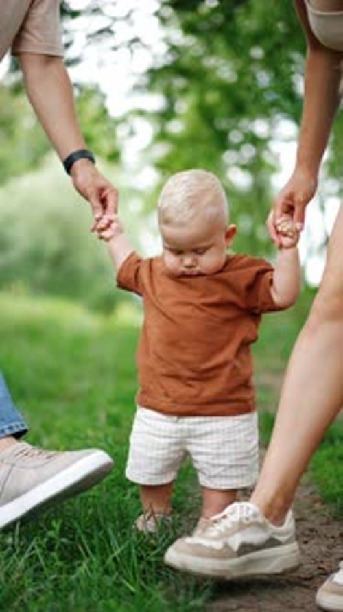 Un precioso bebé que sostiene a sus padres de las manos mira sus pies pisando.