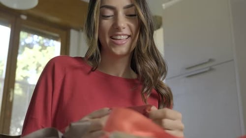 Young Woman Opening a Gift and Smiling Indoors