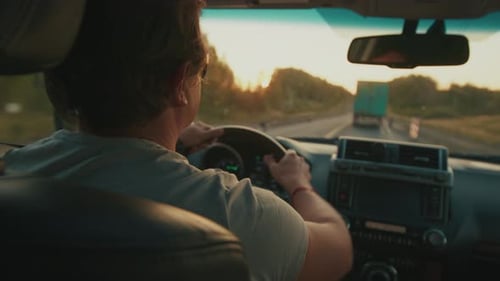 Young Man Steers the Car in Heavy Traffic on the Highway Full of Trucks