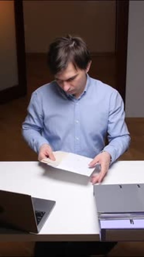 Vertical Video Office Worker Opening Envelope at Desk with Laptop and Files