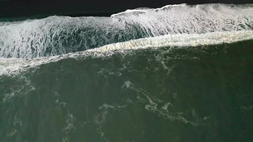 Waves crashing on a black sand beach in Iceland, looking straight down.