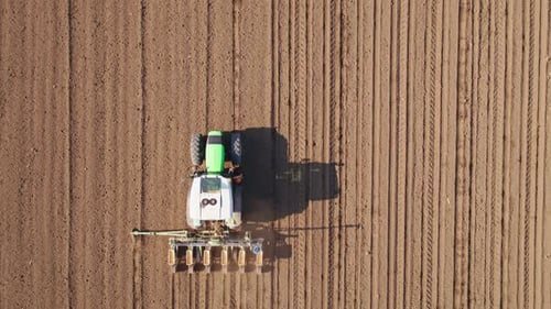 Aerial drone shot of a farmer in tractor seeding, sowing agricultural crops at field.