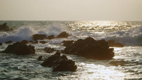 Das Licht des Sonnenuntergangs spiegelt sich auf den Wellen des Ozeans, Felsige Küstenlandschaft, Meerwasser spritzt über Steine und erzeugt