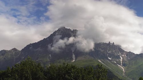 Clouds embracing mountain peak timelapse over lush valley