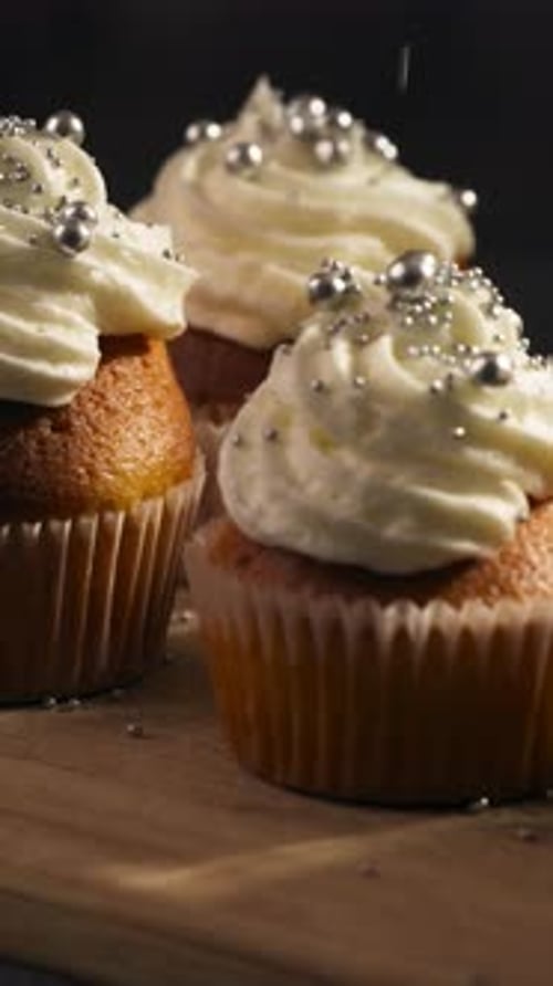 Vertical View Of Cupcakes Topped With Whipped Cream Frosting And Sprinkled With Shiny Pearl Candy.