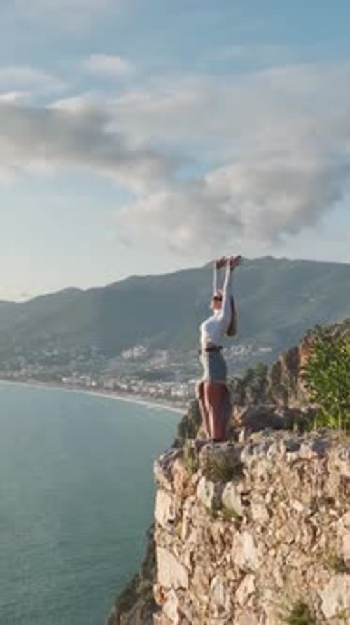 Vertical Video Model Posing Boldly on a Cliff With the Mediterranean s Beauty Behind Her