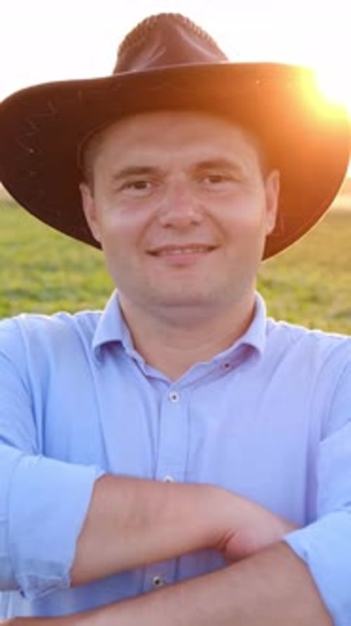 A Happy Farmer in a Straw Hat Smiles at a Beautiful Sunset Above His Lush Green Field
