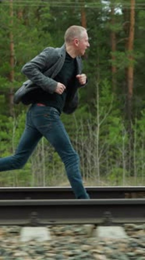 Man in Grey Suit Running on Railway Tracks in Forest