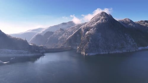 Aerial view of Water dam between snow covered mountains. Reservoir between high mountains.