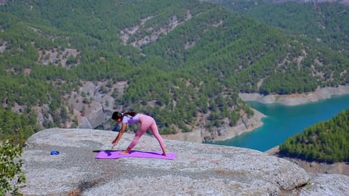 Woman Practicing Yoga on Rock Cliff with Panoramic Mountain and Lake View