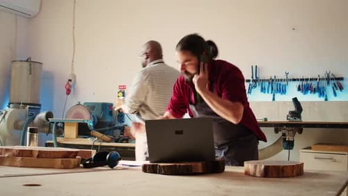 Un menuisier dans un atelier d'assemblage dessine des schémas en parlant sur un smartphone