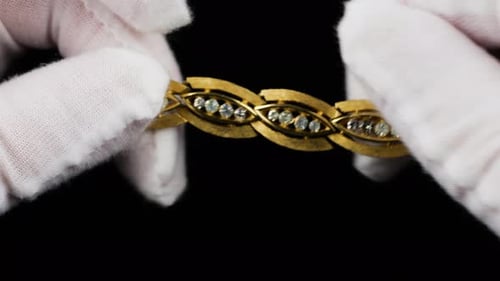 Close-up of vintage gold-tone bracelet being examined in white cotton jersey gloves.