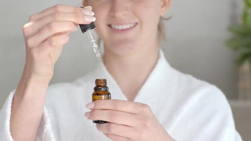 Applying serum with dropper, woman in bathrobe smiling at home