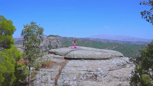 Wide Shot of Woman Practicing Yoga on Cliff with Mountain Landscape