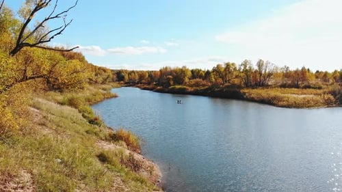 Autumn Landscape with a River and Yellowing Trees Two People are Floating on Surfboards in the River
