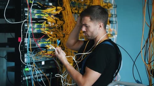 Young man in uniform have a job with internet equipment and wires in server room