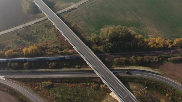 Train passing under a freeway bridge intersection - Aerial top view ...