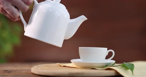 Woman pouring tasty green tea from teapot into cup at wooden table, closeup